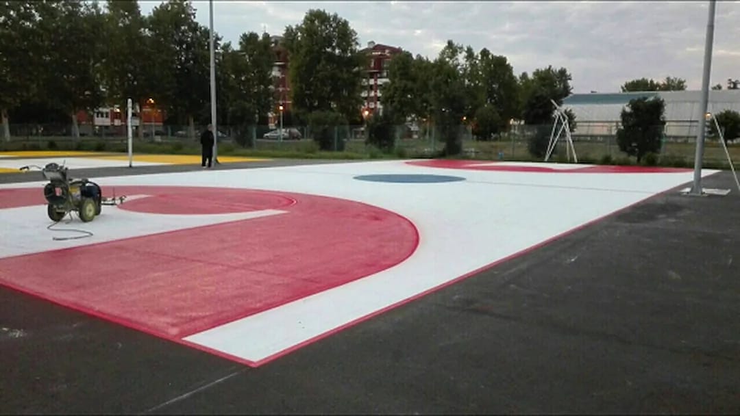 Outdoor sports court being line-marked in red and white with a walk-behind striping machine on site