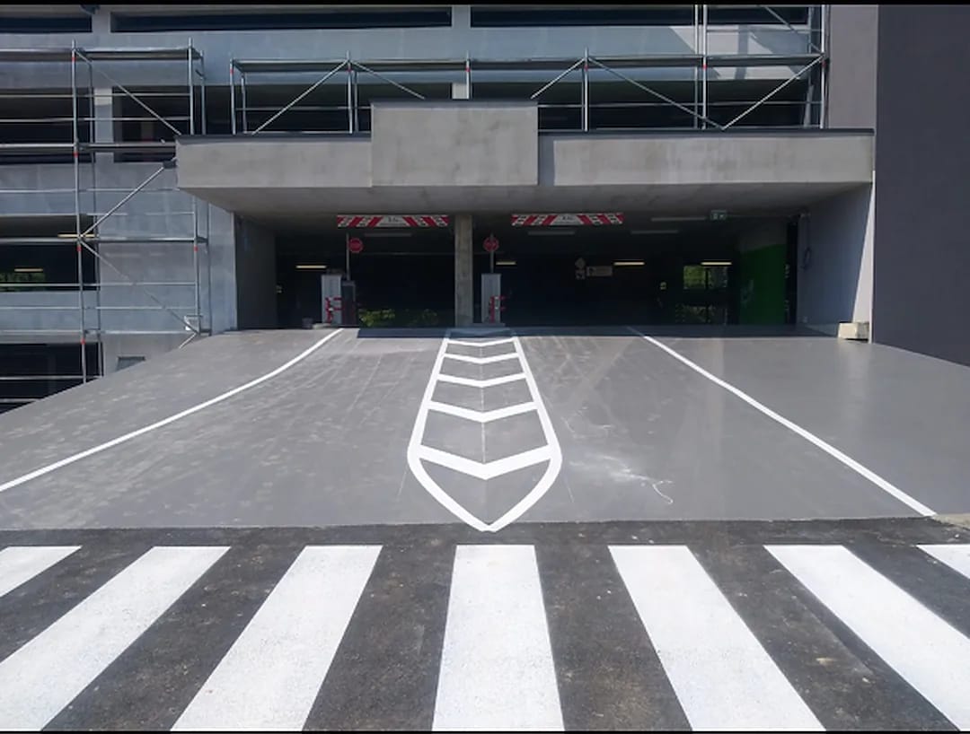 Parking deck entrance with grey deck coating, a bold white chevron marking and a high-contrast crosswalk