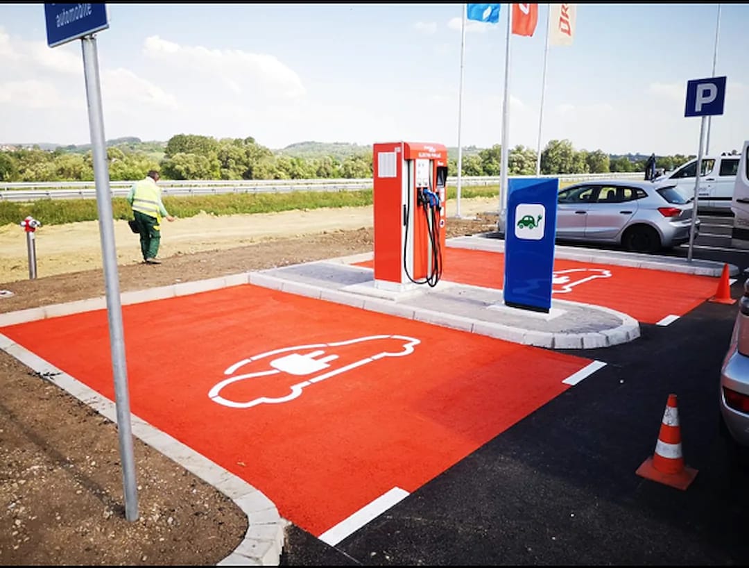Outdoor EV charging bay with a red thermoplastic pad, white electric-vehicle icon and charging unit