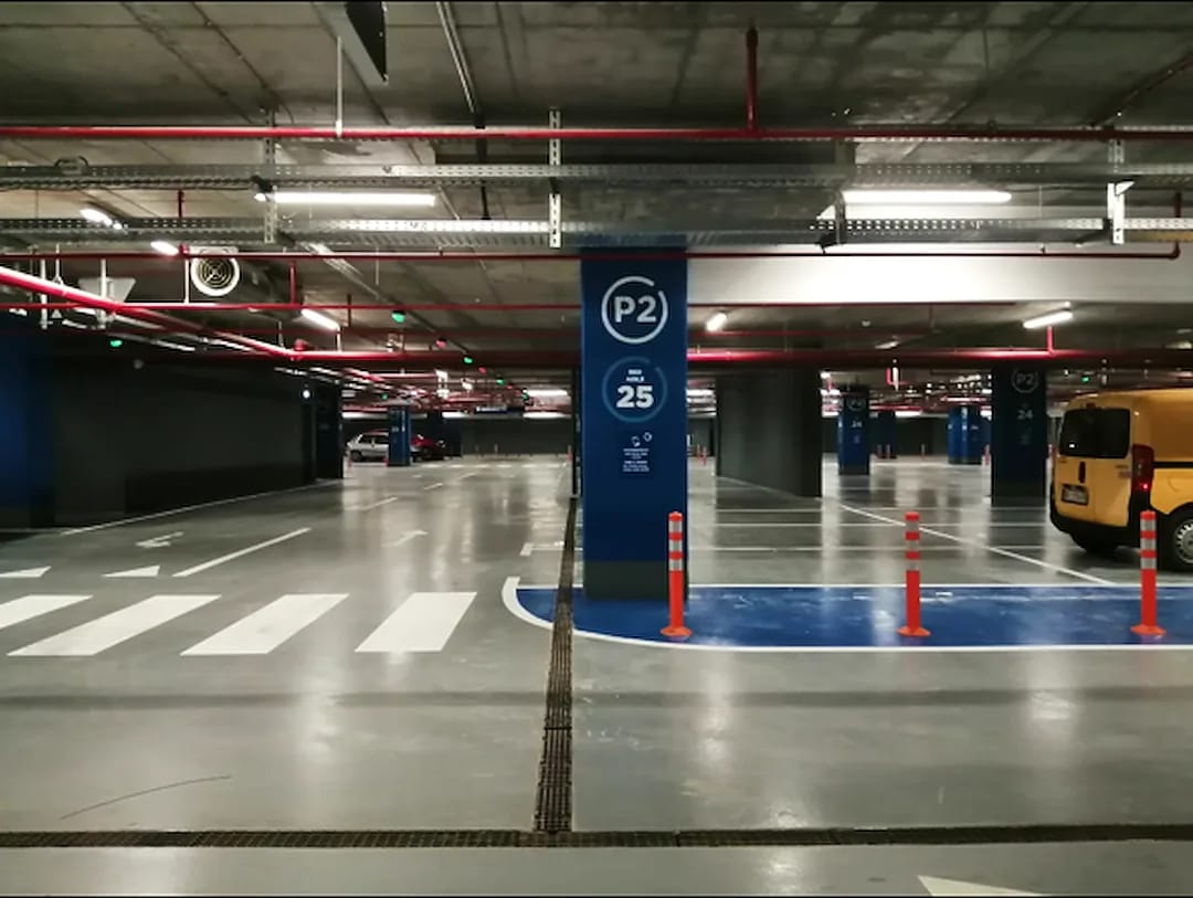 Accessible parking stall marked in blue inside a parking garage with orange delineator posts and a crosswalk