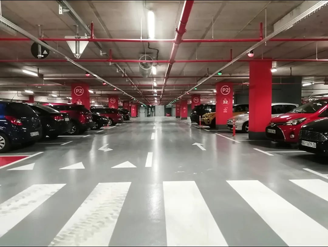 Parking garage interior with white crosswalk stripes, directional arrows and red painted structural columns