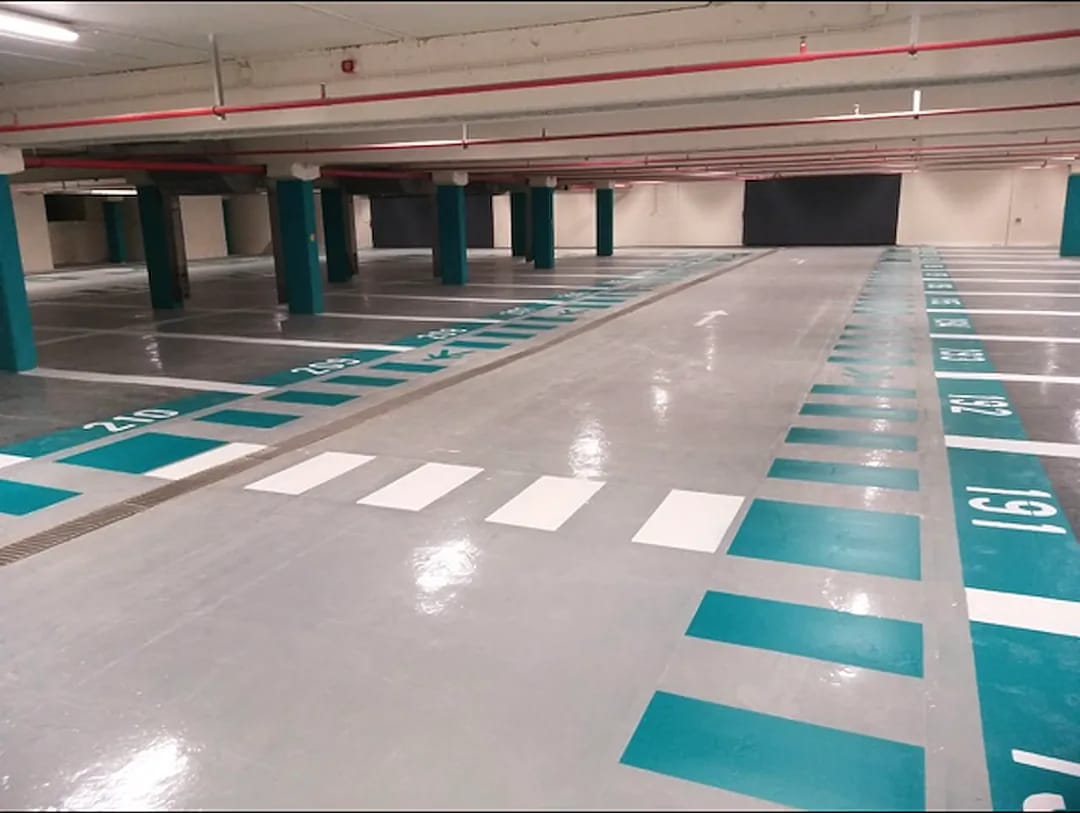 Underground parking garage with teal and white numbered stalls and a white pedestrian crosswalk