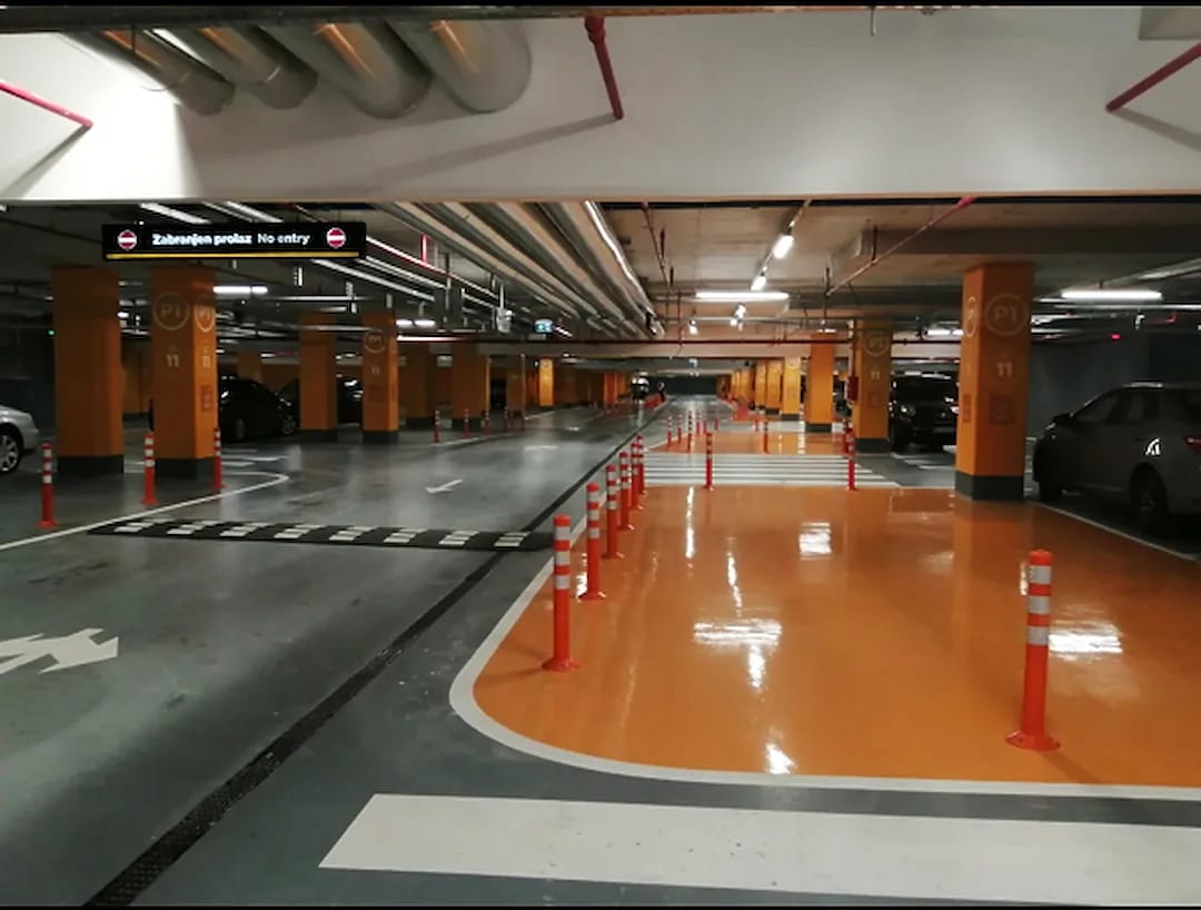 Parking garage with a bright orange epoxy pedestrian walkway, orange bollards and a speed bump