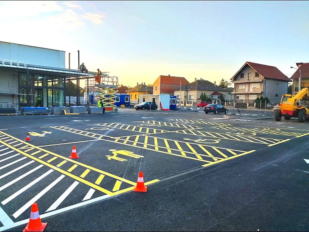 Large commercial lot at dusk with extensive yellow hatching, multiple ADA symbols and traffic cones during layout work